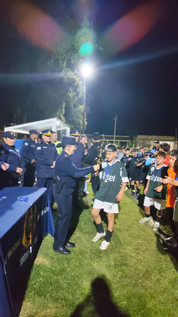 Una oficial de policía le entrega un trofeo a un niño futbolista. Entrega de trofeos.