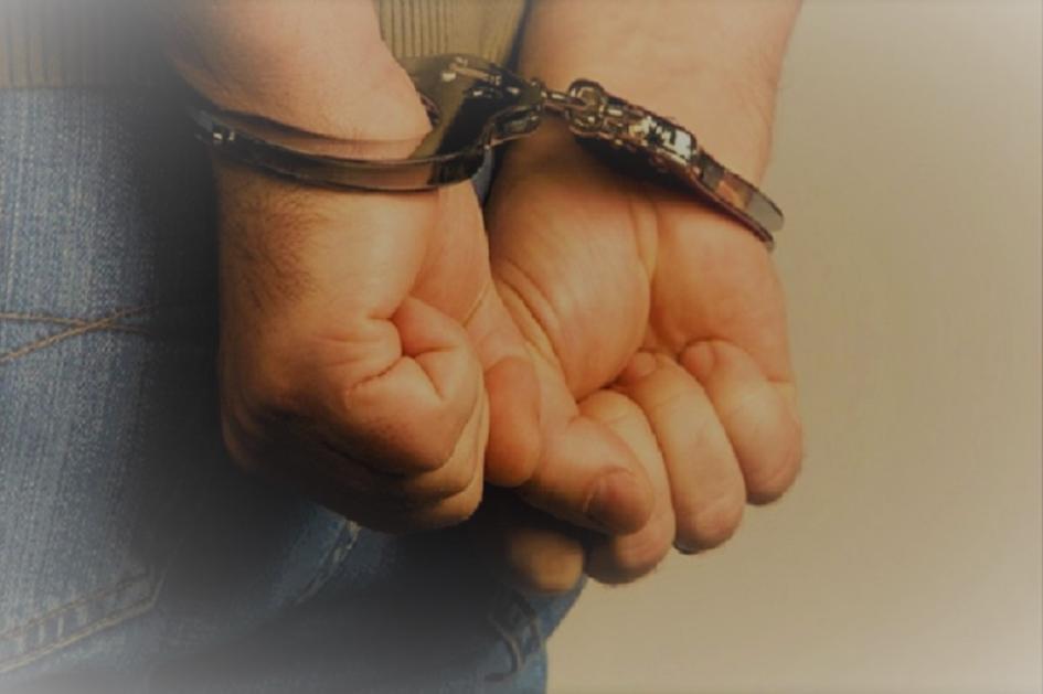 Hombre detenido por personal policial. Manos con esposas.
