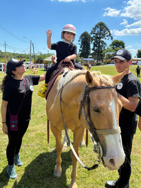 Niña a caballo acompañada por dos adultos mientras saluda con la mano en un campo soleado. Niña a caballo acompañada por dos adultos mientras saluda con la mano en un campo soleado.