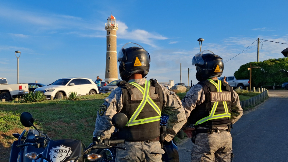 Dos policías de la Unidad PUMA frente a un faro costero con autos alrededor.
