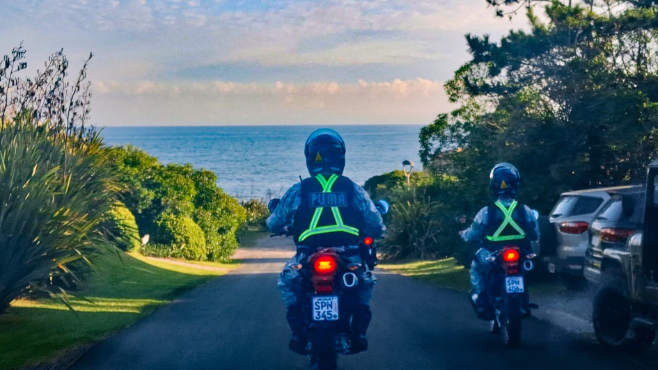 Dos policías de la Unidad PUMA en moto descienden hacia la costa con el mar de fondo.
