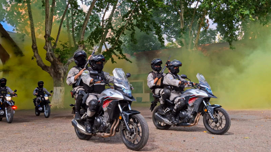 Equipo PUMA en motocicletas avanza en formación, con armas largas, entre humo de color