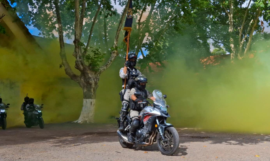 Policías PUMA en moto con estandarte avanzan entre humo de color en zona arbolada