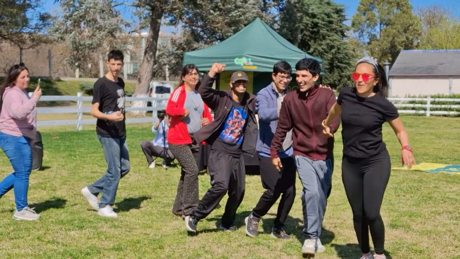 Personas riendo y haciendo una fila sobre el pasto frente a una carpa verde de COPOL..