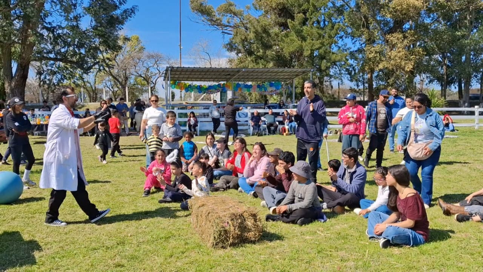 Persona con bata blanca haciendo una presentación frente a adultos y niños sentados en el pasto.