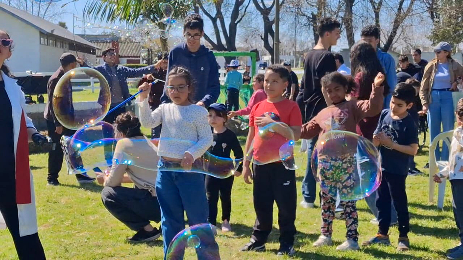 Varias niñas y niños atrapan y hacen flotar burbujas de jabón de colores al aire libre