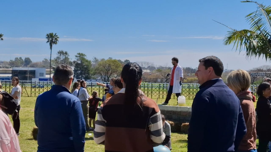 Autoridades asistentes de espaldas miran una actividad en un espacio abierto rodeado de árboles.