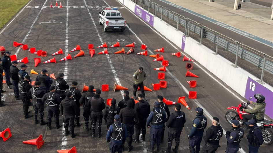 Policías agrupados en una pista de carreras observan una demostración rodeados de conos naranjas.