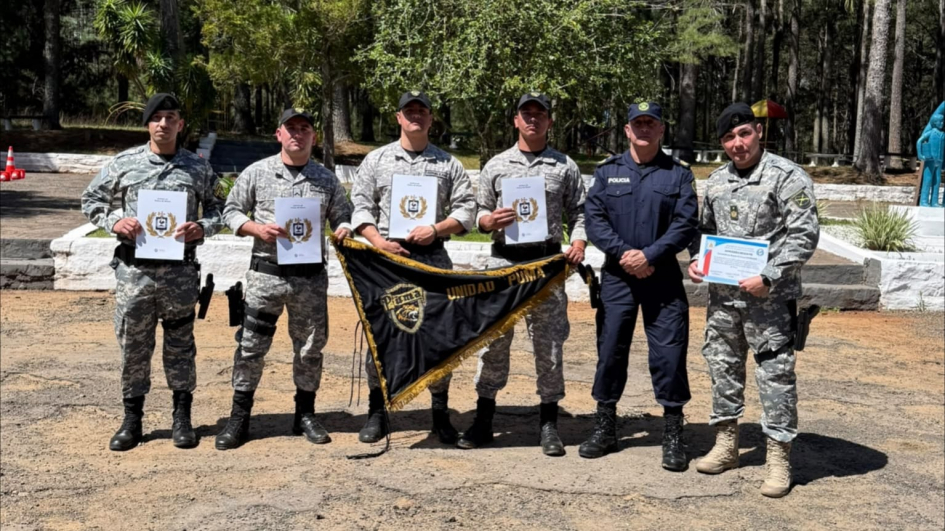 Seis efectivos posan de frente mostrando sus diplomas y sosteniendo el estandarte de la Unidad Puma.