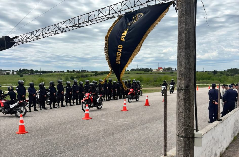 Agentes en motos avanzan en pista bajo el estandarte Unidad PUMA, observados por superiores