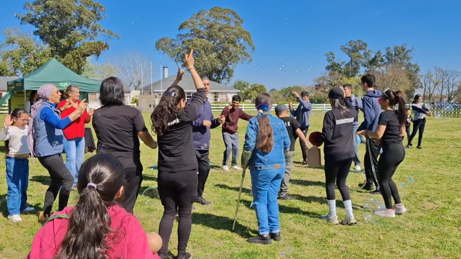 Grupo de personas tomadas de las manos o bailando juntas al aire libre en un día soleado.