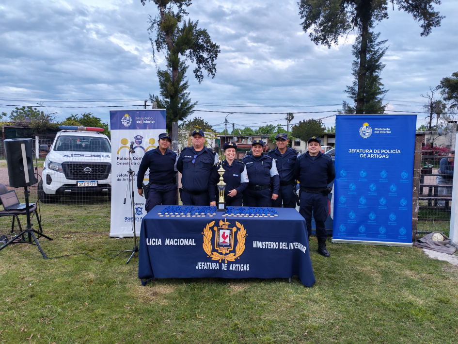 Personal de la Oficina Comunitaria Orientada a Problemas posa rente a una mesa Personal de la Policia Comunitaria