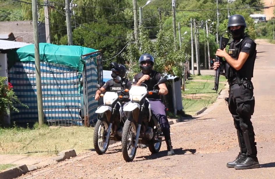 Operativo de Brigada Departamental Antidrogas Dos policías sentados, cada uno sobre una moto, y un policía parado en la calle con un arma larga