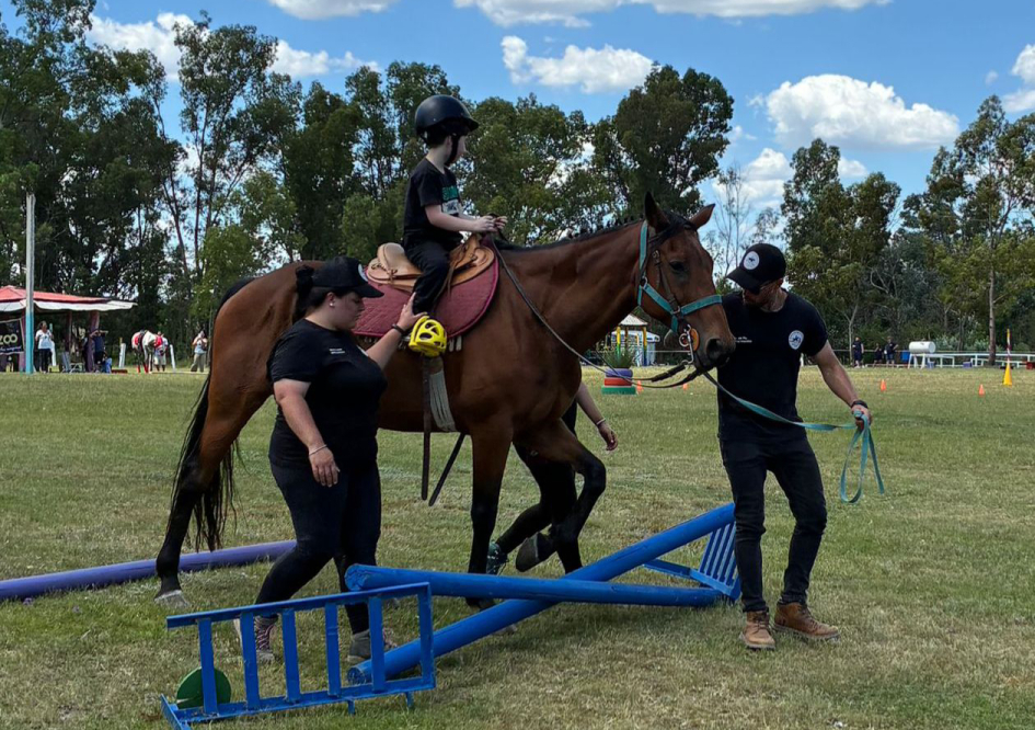 Niño a caballo guiado por dos adultos mientras el animal cruza un pequeño obstáculo. Niño a caballo guiado por dos adultos mientras el animal cruza un pequeño obstáculo.