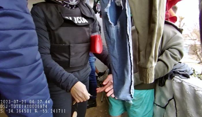 Policía colocando esposas a detenido entre ropas tendidas