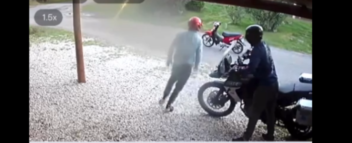 dos personas con casco, paradas al costado de una moto
