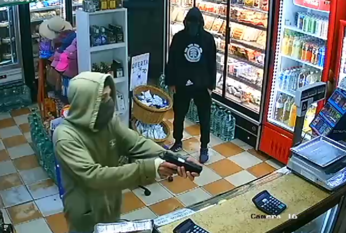 una hombre apuntando con un arma dentro de un comercio