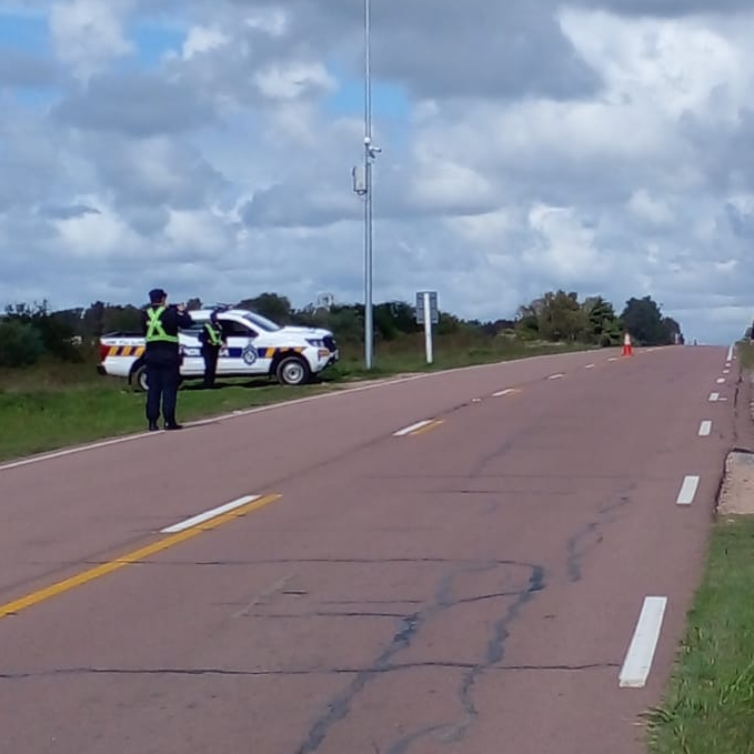 dos policías parados al costado de una camioneta policial, cerca de una ruta