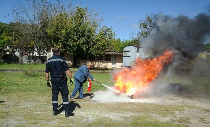 participante de curso de bomberos usando un extintor para apagar el fuego.