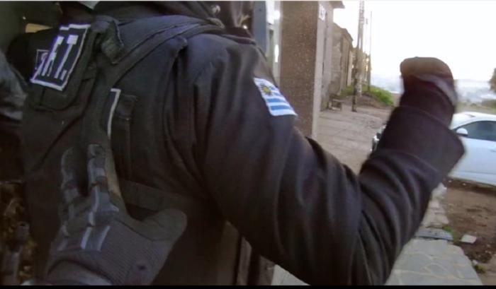 Policía de negro ingresando a allanamiento y su compañero lo impulsa con su mano izquieda de atrás Policías ingresando a allanamiento