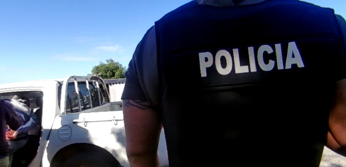 Policia de espalda y detenido ingresando esposado a un móvil