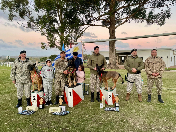 Podio de premios 1er, 2do y 3er puesto con binomios DNGR Policías de la DNGR con canes ganadores en podio, acompañados por oficiales