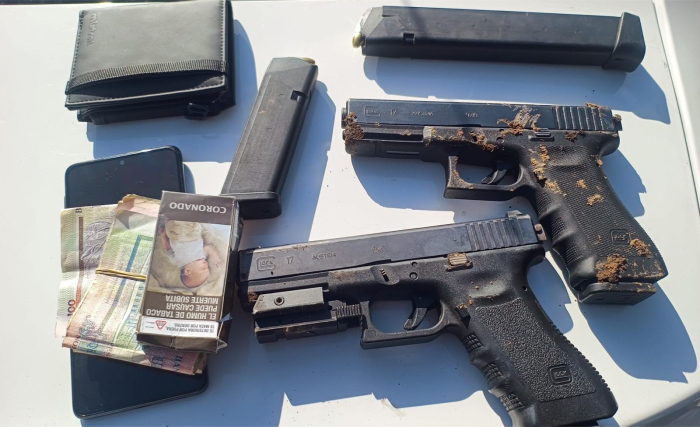 Pistolas Glock, cargadores, teléfono celular, dinero incautados exhibidos en una mesa