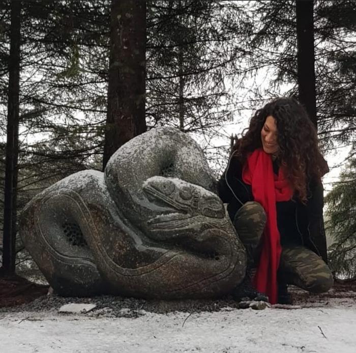 Uruguayan artist Gissella García posing next to one of her stone sculptures, with a snowy landscape 