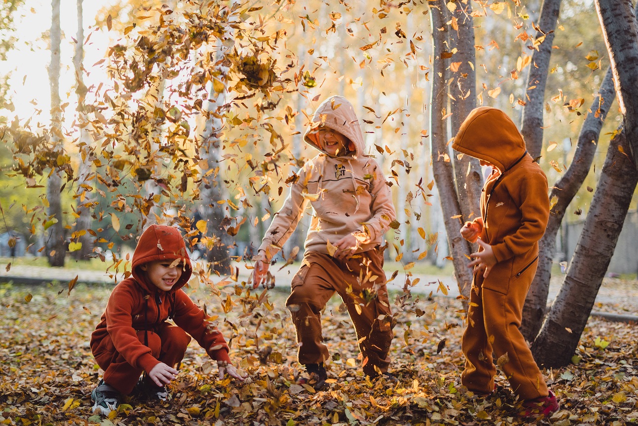 Niños juegan en un parque tirando al aire hojas caídas de los árboles