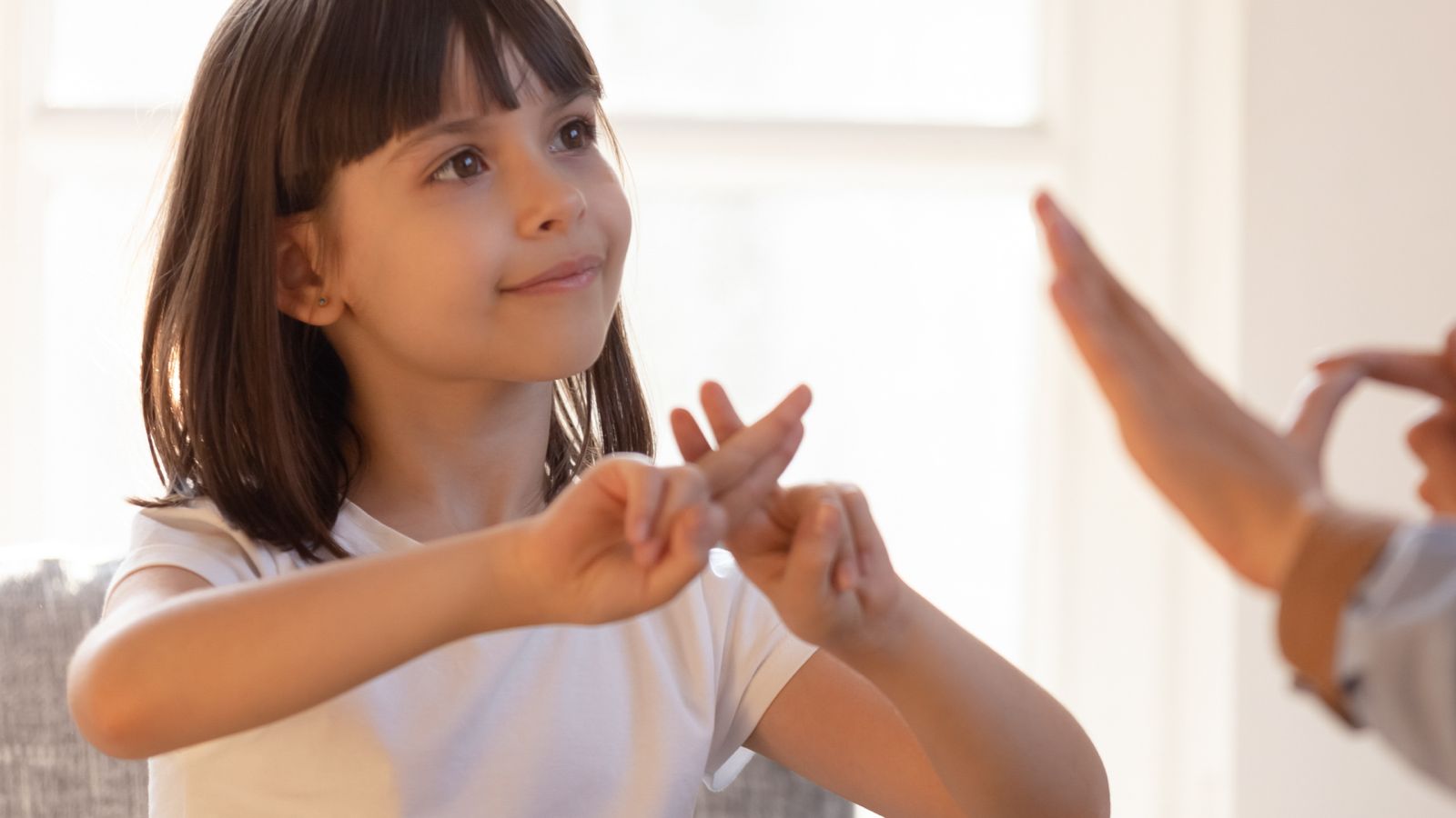 Niña hace una seña con su mano y se ve otra mano que hace otra seña