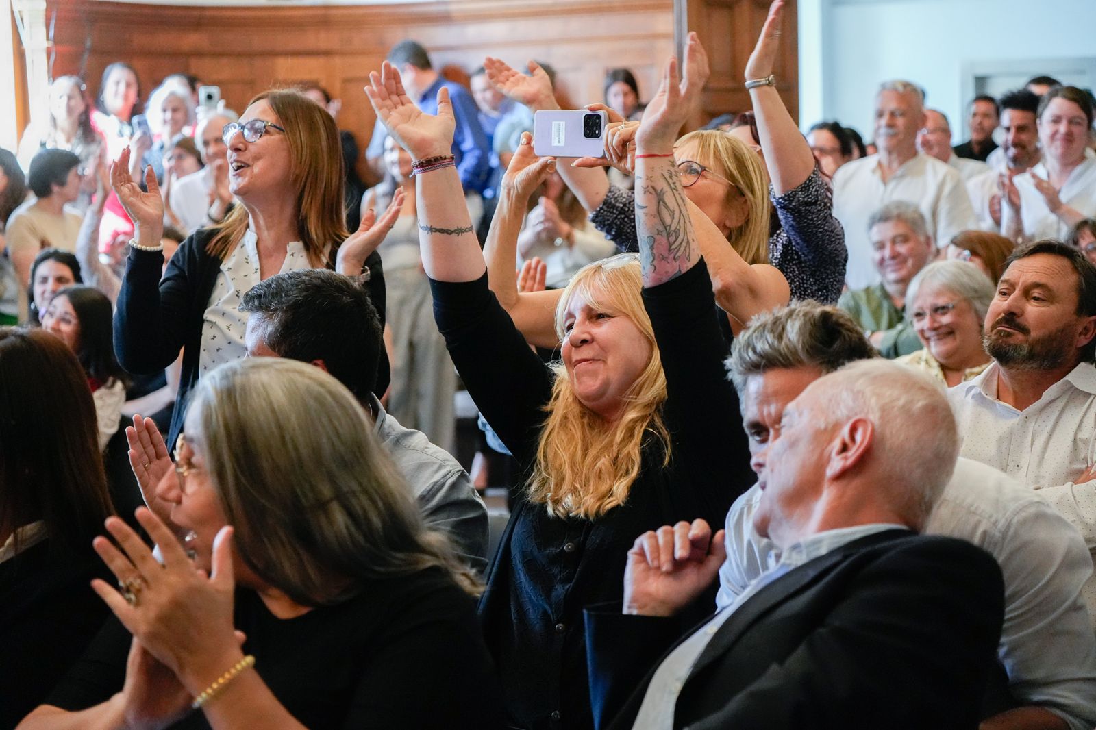 Funcionarias y funcionarios alegres. Una levanta sus manos, otra aplaude, otros sentados y de pie