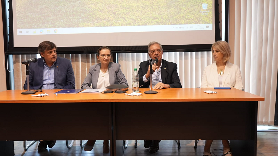 Cuatro autoridades sentadas detrás de una mesa, con un proyector de fondo