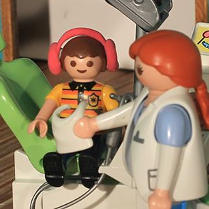 niño escucha música mientras la dentista le acerca un babero