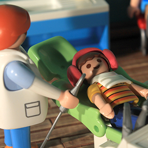 niño sentado en el sillón, con babero y auriculares puestos, mientras la dentista trabaja con uno de sus instrumentos