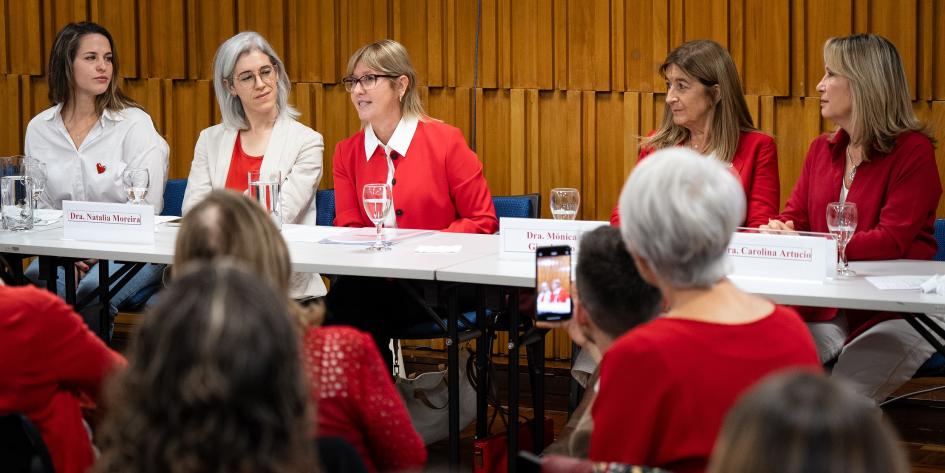 Ministra en acto conmemorativo La Ministra habla. Las mujeres de la mesa de autoridades y público la miran con atención.