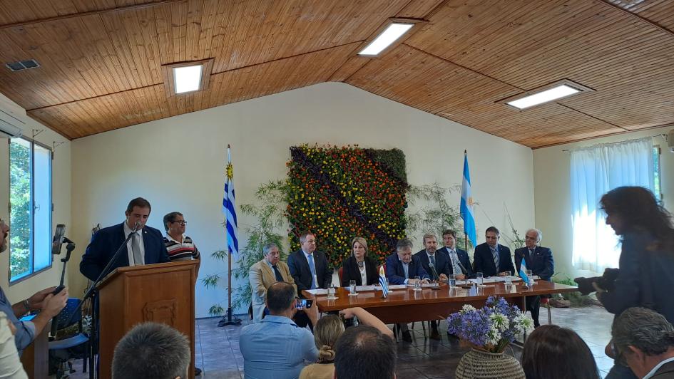 Mesa de trabajo en salud Fray Bentos- Gualeguaychú Mesa con 8 autoridades, una persona habla desde un atril. Al fondo banderas de Uruguay y Argentina