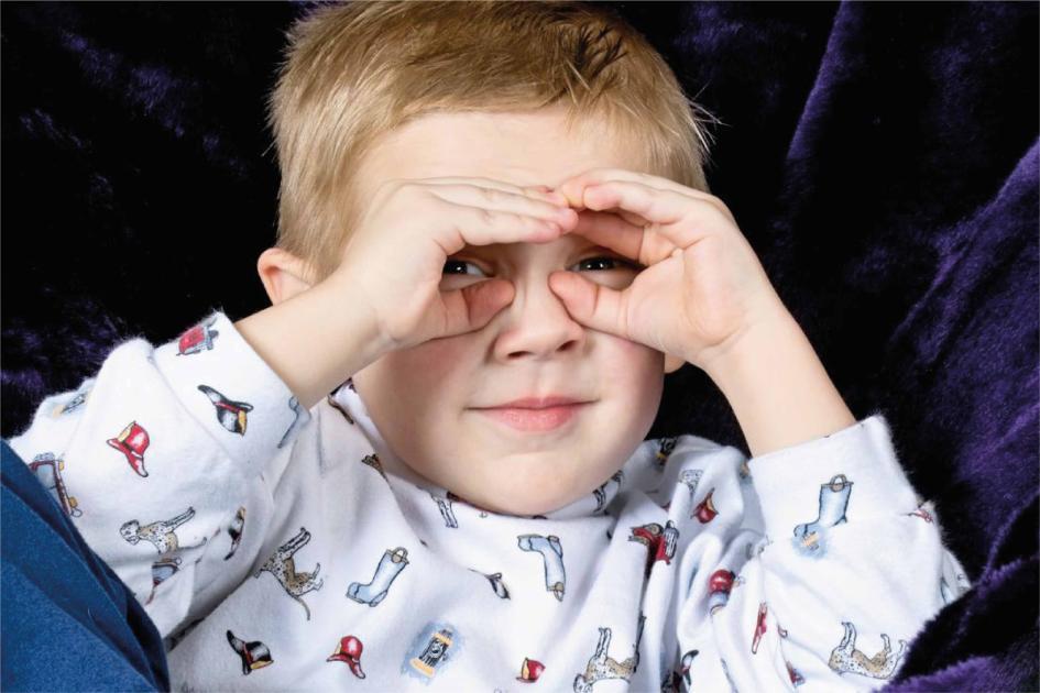 Día mundial de la visión Niño pequeño con pijama hace gesto de binoculares con sus manos