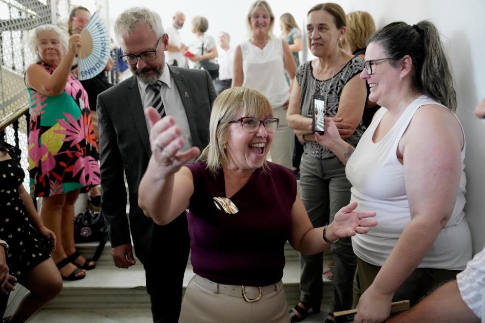 Llegada Lustemberg y Briozzo descienden por escalera, rodeados de personas. Ella sonríe y extiende brazos