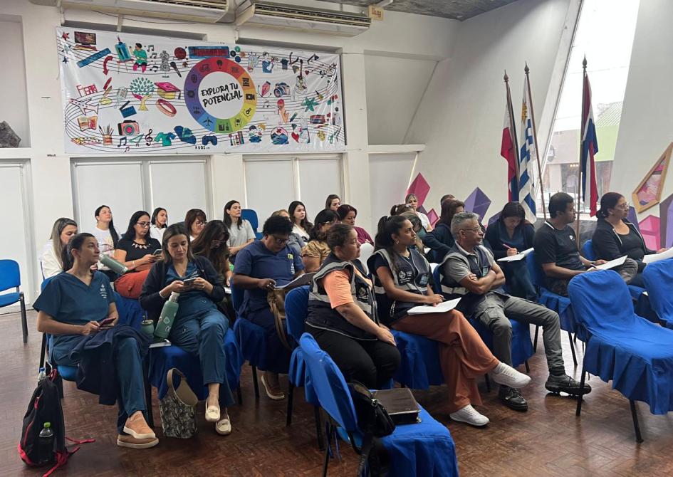 Personal de salud del primer nivel de atención Mujeres y hombres con uniformes sentados en sillas, miran hacia las exponentes.