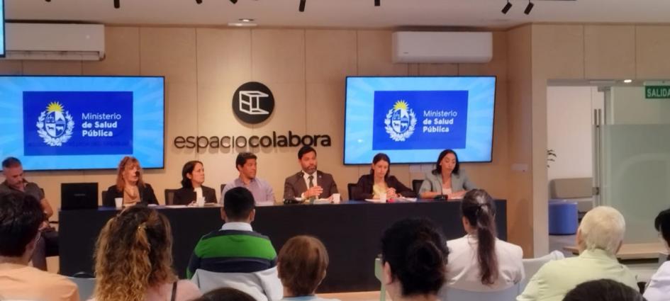 Día Mundial del Paciente Celíaco en Espacio Colabora Asistentes sentados, de espaldas a cámara, al fondo de la imagen la mesa con expositores y pantallas
