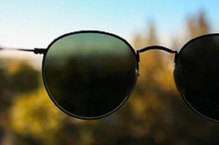 imagen de unos lentes de sol con un fondo de arboles y cielo