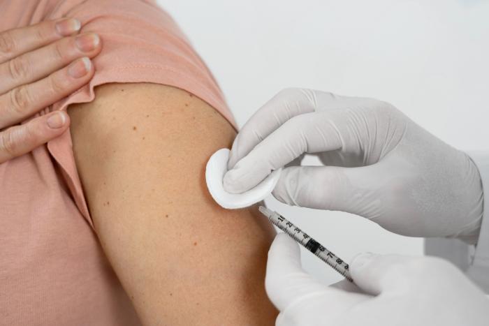 Manos con guantes presionan con algodón el sitio de inyección y con la otra vacuna el brazo de mujer