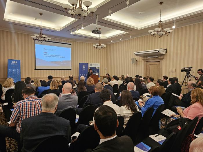 Sala cerrada con asistentes sentados, al fondo, de pie, la Ministra se dirige al público
