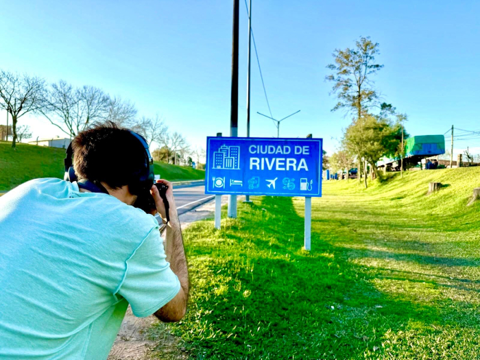 Ingreso a la ciudad de Rivera Persona de espaldas toma foto a un cartel en la ruta que dice ciudad de Rivera