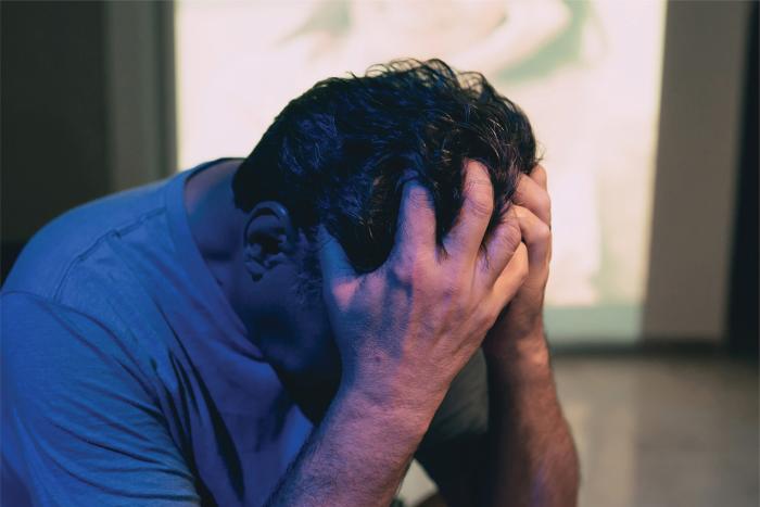 Hombre adulto cabizbajo se agarra la cabeza con las manos