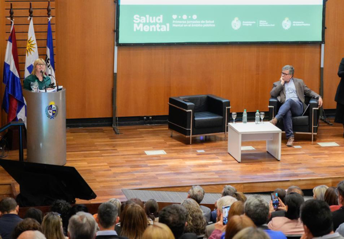 Ministra en escenario de pie detrás de un atril da un discurso al público sentado