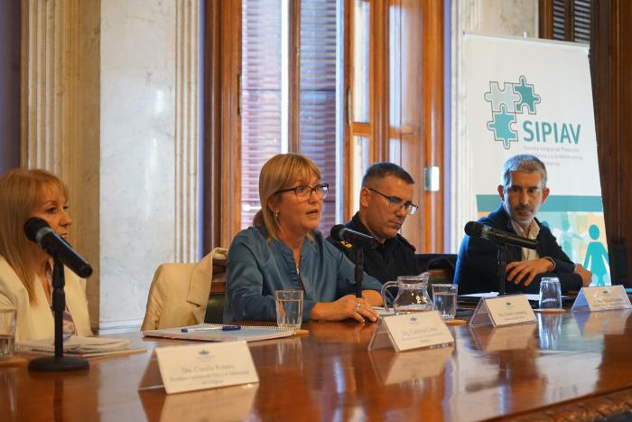 Presentación de datos del SIPIAV Cristina Lustemberg, junto a 3 autoridades, habla al micrófono. Al fondo un roll up del SIPIAV