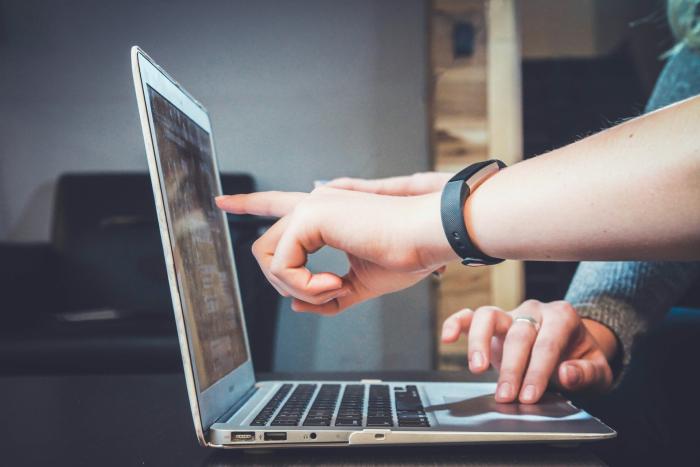 Mano de mujer señala pantalla de una computadora portátil mientras otra usa el trackpad