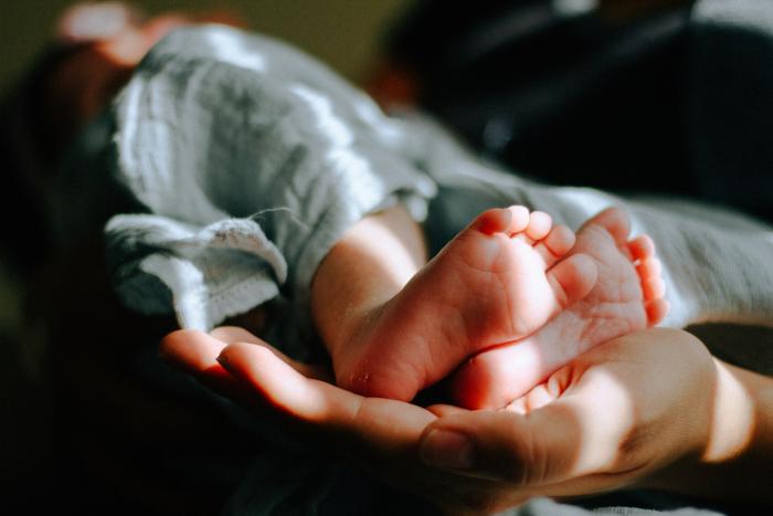 Bebé sostenido por un adulto Mano de una persona adulta sostiene los pies de un bebé recién nacido