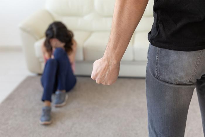 Hombre apretando puño mientras mira a una mujer sentada en el piso Hombre apretando puño mientras mira a una mujer sentada en el piso